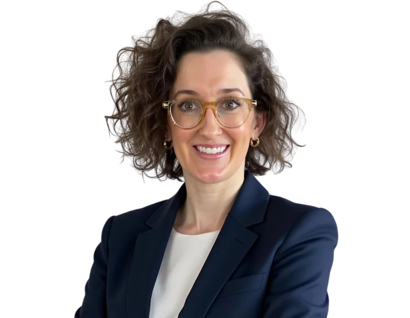Lindsey Stewart smiling confidently with curly brown hair, wearing clear-framed glasses, gold hoop earrings, and a navy blazer over a white blouse against a plain background.