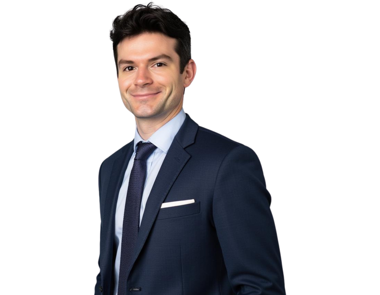 Professional headshot of Benjamin Rowley smiling, wearing a navy blue suit with a white dress shirt, dark tie, and pocket square, posed against a softly blurred light background.