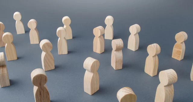 Several small wooden figurines shaped like simplified human figures are arranged on a gray surface. The scattered positioning suggests concepts of community, networking, or social distancing.