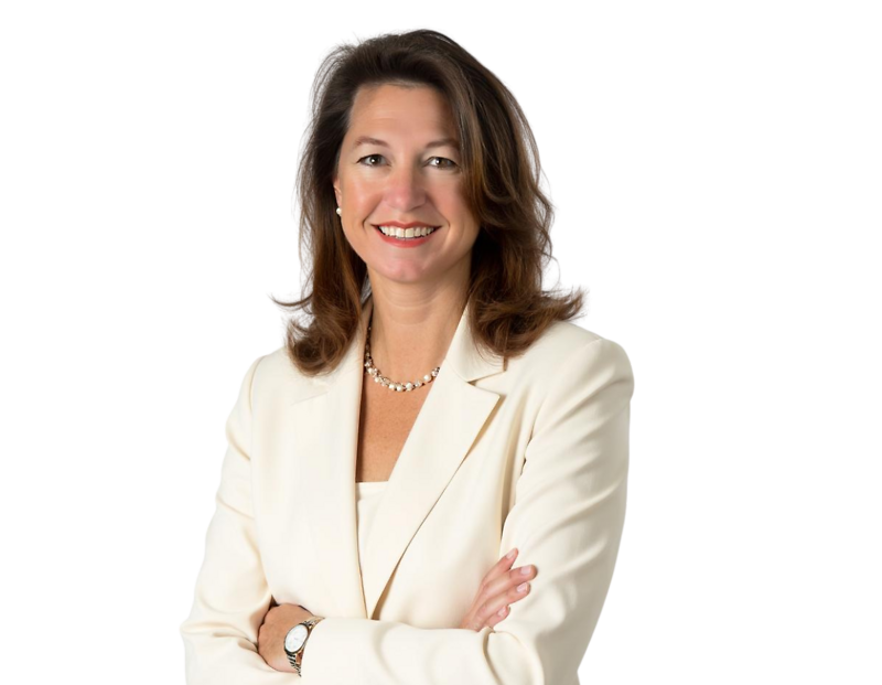 Professional headshot of a woman with shoulder-length brown hair, wearing a white blazer, pearl necklace, and a confident smile. She stands with her arms crossed against a white background, giving a poised and professional impression.