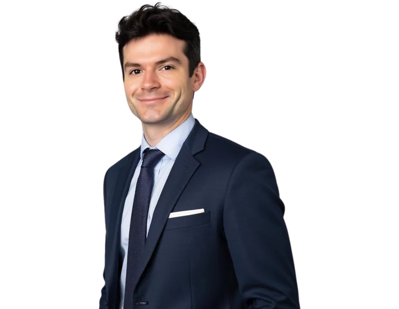 Professional headshot of Benjamin Rowley smiling, wearing a navy blue suit with a white dress shirt, dark tie, and pocket square, posed against a softly blurred light background.
