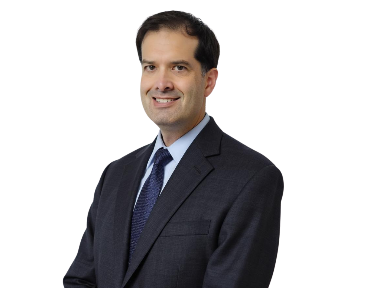 Colin Thakkar in a dark suit and blue tie stands smiling against a modern blue and white geometric background.