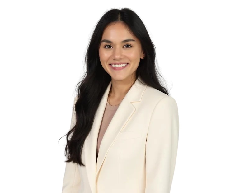 Smiling woman with long dark hair wearing a cream-colored blazer over a beige top. She is facing forward against a transparent background.