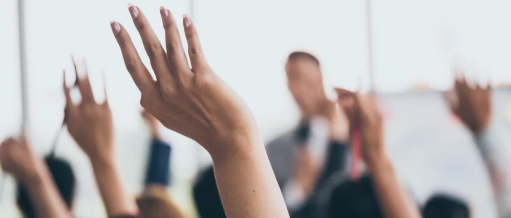 Audience raising hands up while businessman is speaking in training at the office.
