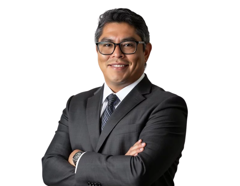 Professional man with short, dark hair wearing glasses and a dark gray suit with a striped tie, smiling with arms crossed. He stands confidently against a plain white background, presenting a polished and approachable corporate image.