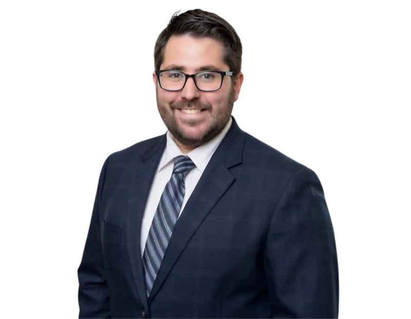 Smiling man with dark hair, beard, and glasses wearing a dark plaid suit, white shirt, and striped tie. He is standing against a transparent background.