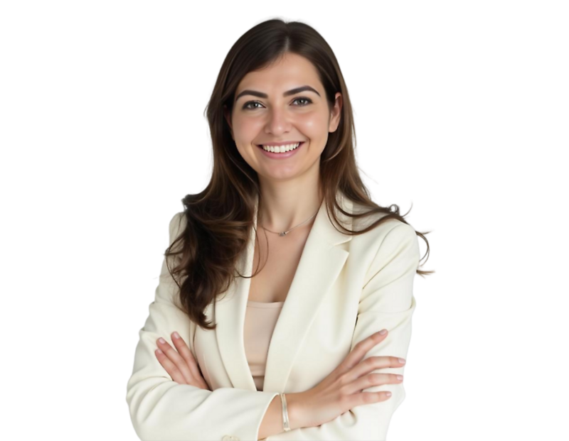 A confident young woman with long brown hair smiles while standing with her arms crossed. She is dressed in a cream-colored blazer over a beige top, giving a professional and approachable appearance.