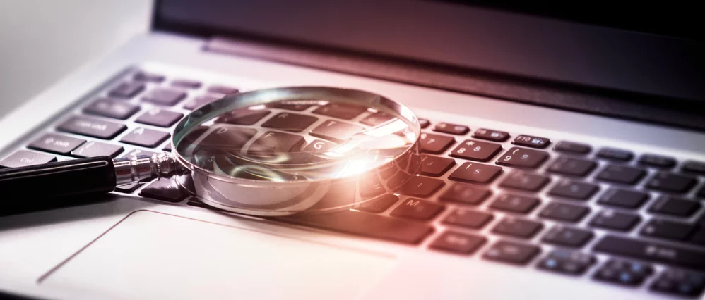 Magnifying glass on laptop keyboard search the internet for online documents background