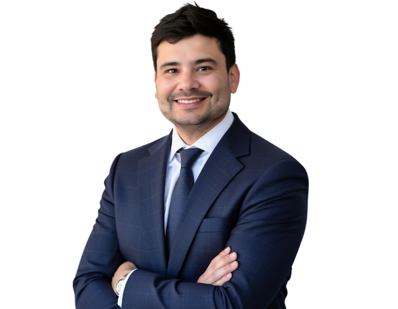 A man with short dark hair and a trimmed beard smiles confidently while wearing a dark blue checkered suit, white shirt, and navy tie. He stands against a transparent background with his arms crossed, exuding professionalism and approachability.
