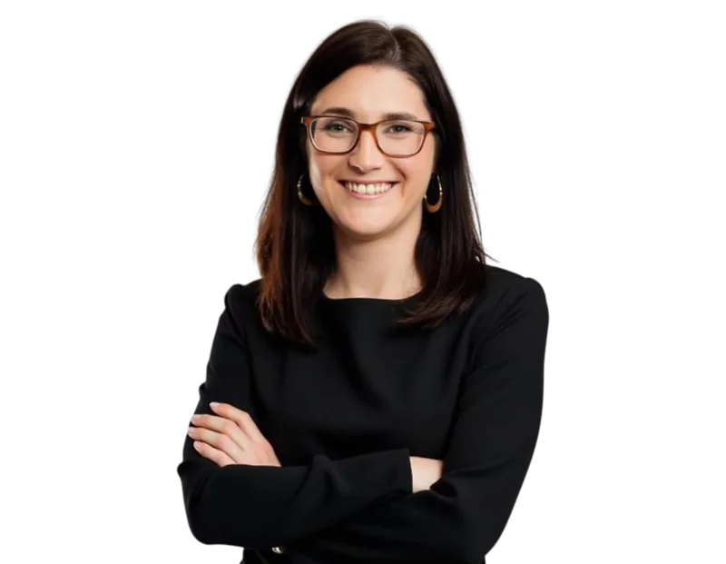 Woman with straight dark brown hair wearing glasses, gold hoop earrings, and a black long-sleeve dress, smiling with arms crossed against a transparent background.