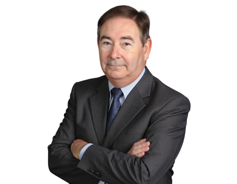 Rick Brown in a dark gray suit and blue tie standing with arms crossed, looking confidently at the camera against a transparent background. His expression is calm and professional, suggesting a business or executive portrait.