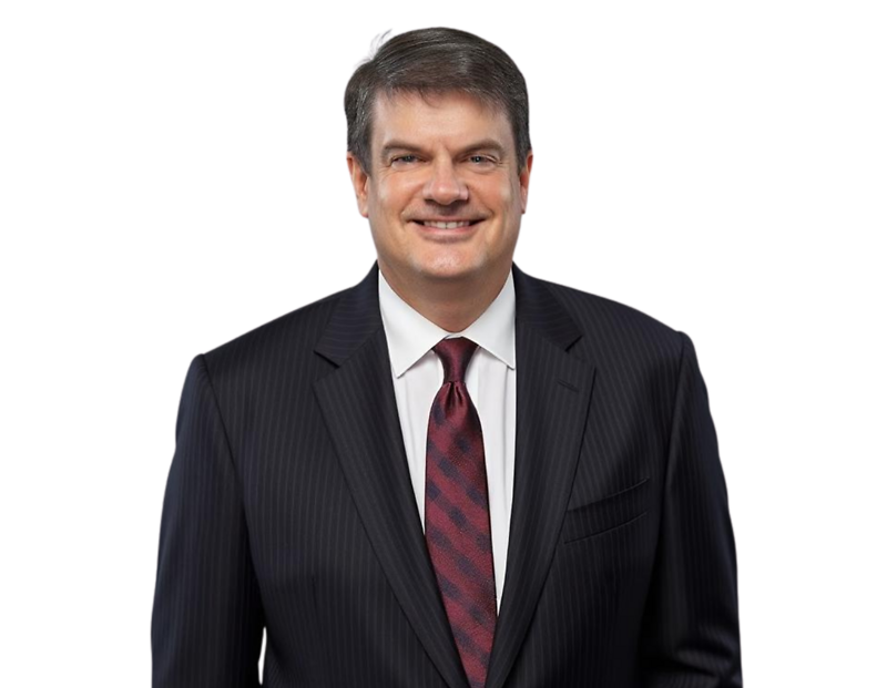 A professional headshot of a man wearing a dark pinstripe suit, white dress shirt, and a maroon patterned tie, smiling confidently. The background has been removed, making the image suitable for corporate profiles or executive bios.