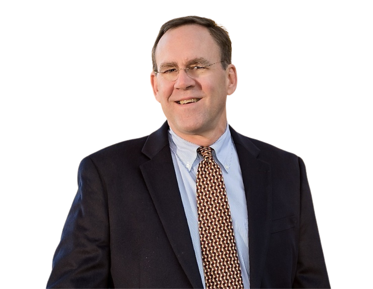 Jim Coleman in a dark blazer, light blue button-down shirt, and a geometric patterned tie, standing confidently against a transparent background. His relaxed posture and business attire convey a professional yet approachable demeanor.