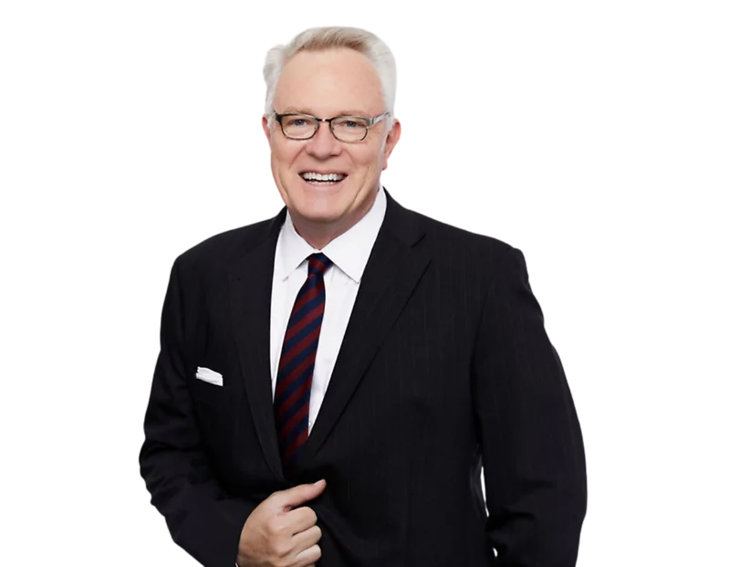 Terry Higham smiling in a dark pinstripe suit with a white shirt and red-and-navy striped tie, wearing glasses and standing against a transparent background in a professional headshot.