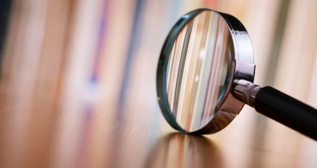 Magnifying glass on table with colorful books out of focus