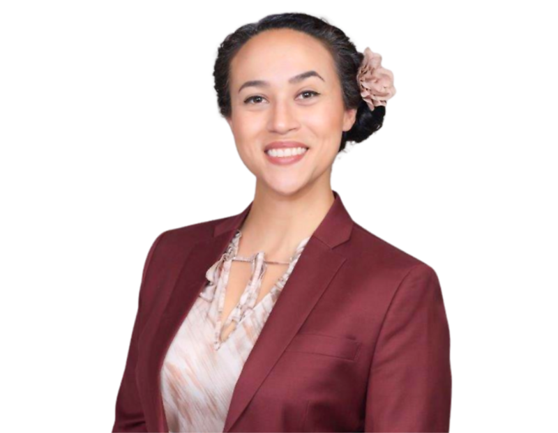 Arcelia Magaña wearing a burgundy blazer over a patterned blouse, with their dark hair styled back and adorned with a light pink flower, posed in front of a blue and white geometric background.