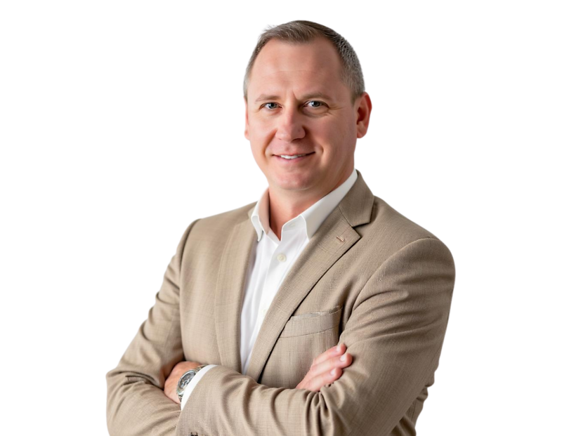 Jesse Bannon wears a beige suit jacket over a white shirt, smiling with arms crossed against a light blue and white geometric background.