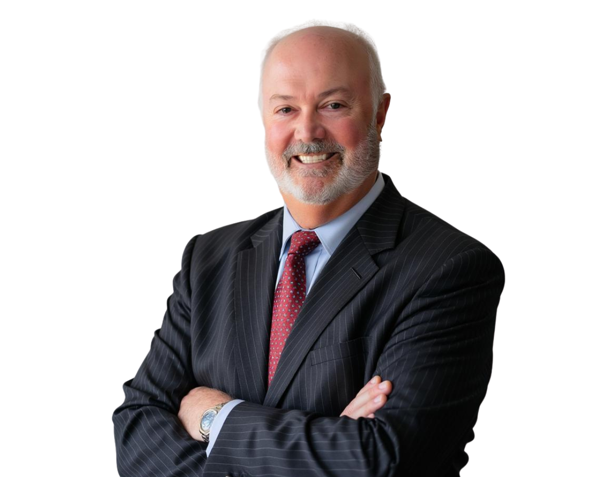 Smiling man with a gray beard and bald head wearing a dark pinstripe suit, light blue shirt, and red patterned tie. He is standing with arms crossed against a transparent background.