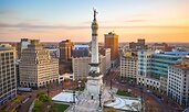 Aerial view of Monument Circle in downtown Indianapolis, Indiana, at sunset. The Soldiers and Sailors Monument stands at the center, surrounded by historic and modern buildings along the circular roadway.