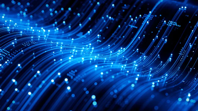 Abstract digital illustration of glowing blue light trails and particles flowing across a dark background, representing high-speed data transfer or fiber-optic network connections. The curved streaks create a sense of motion and advanced technology.