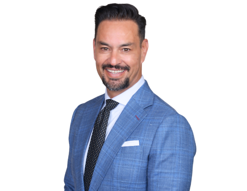 Guillermo Escobedo in a light blue plaid suit jacket, white shirt, and black polka-dot tie smiles against a light blue and white geometric background.