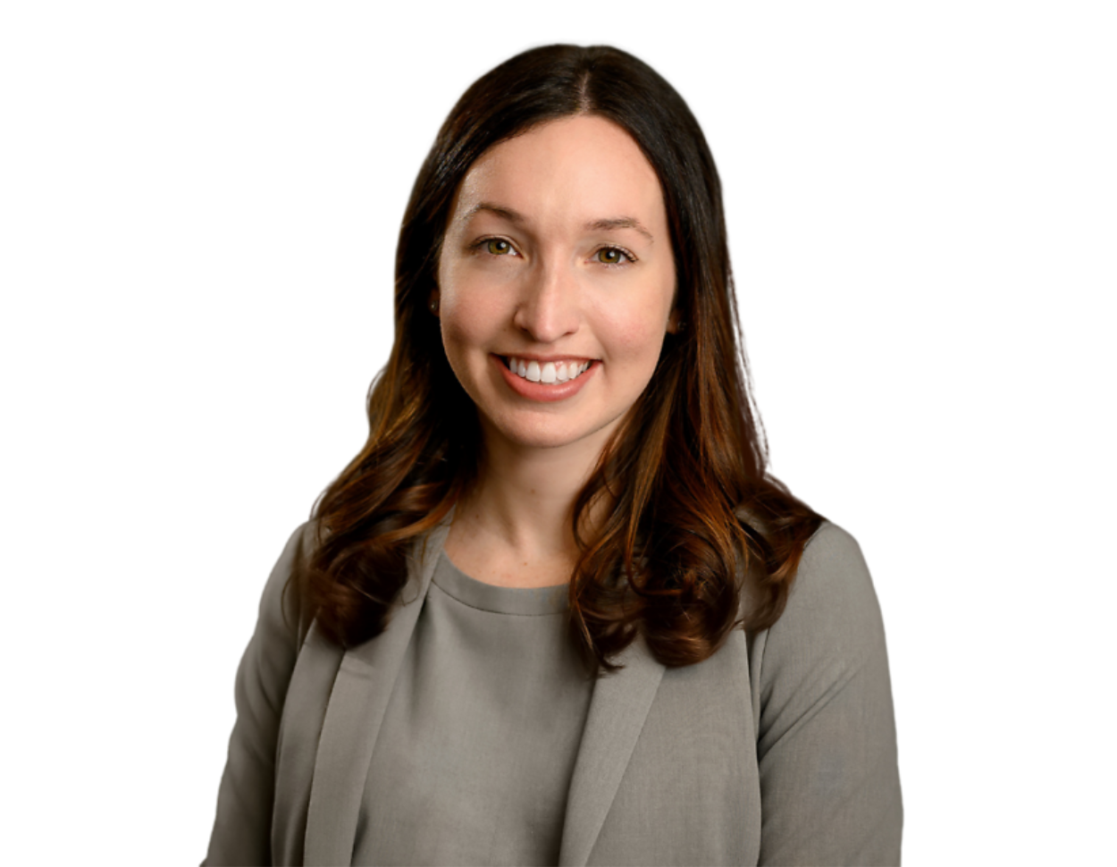 A professional headshot of a woman with long, wavy brown hair wearing a gray blazer and a matching blouse, smiling at the camera. The background has been removed, isolating her against a transparent backdrop, making it ideal for business or corporate use.