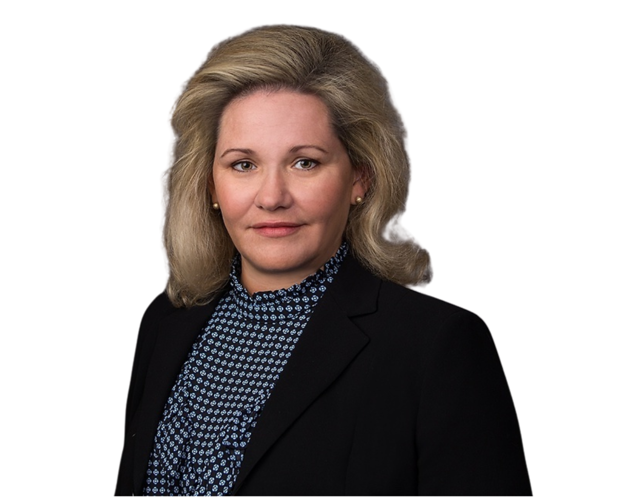 Professional woman with voluminous blonde hair wearing a black blazer over a patterned navy blouse, posed against a transparent background. Her composed expression and formal attire suggest a corporate or leadership role.