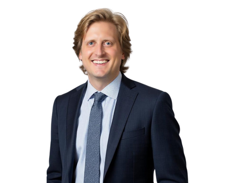 Evan Jarrold smiling in a dark navy suit with a light blue shirt and patterned tie, posed against a transparent background in a professional headshot style.