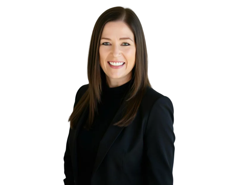 Katie Kelley smiling while standing, wearing a black blazer and top, with straight brown hair against a transparent background.