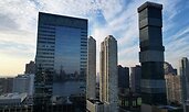 Morning view of Jersey City, New Jersey, with modern glass skyscrapers reflecting the skyline. Wispy clouds stretch across a blue sky above the urban landscape.