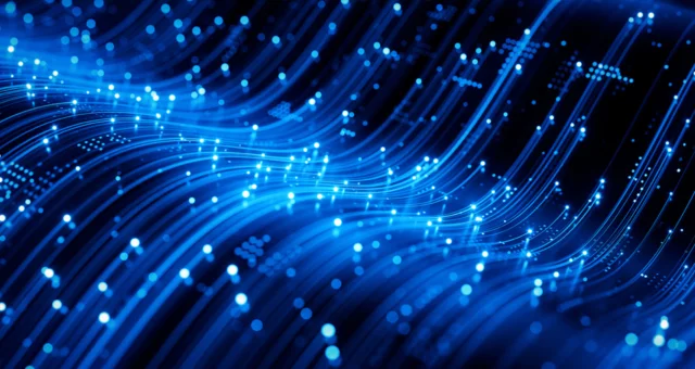 Abstract digital illustration of glowing blue light trails and particles flowing across a dark background, representing high-speed data transfer or fiber-optic network connections. The curved streaks create a sense of motion and advanced technology.