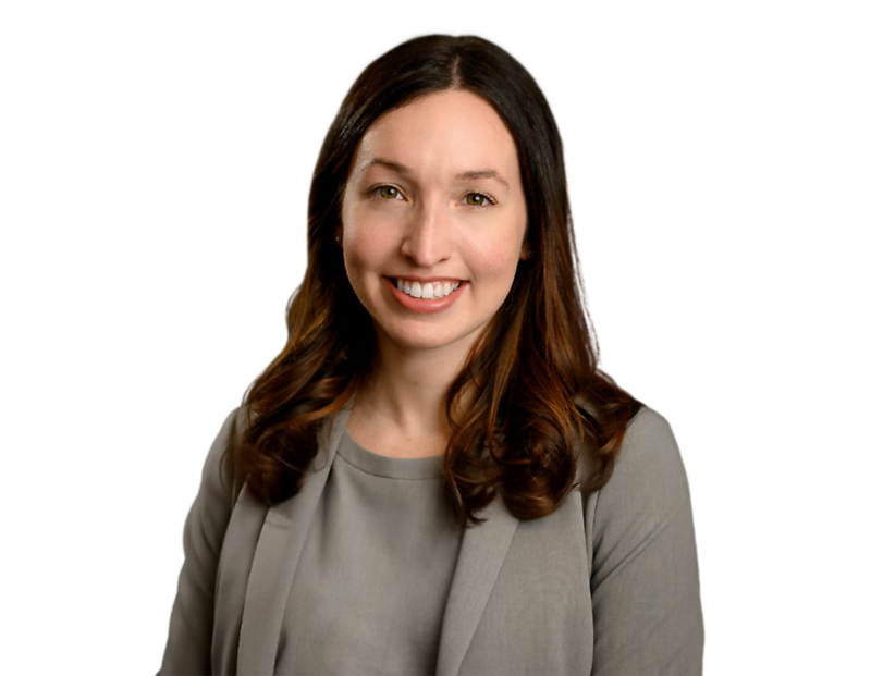 A professional headshot of a woman with long, wavy brown hair wearing a gray blazer and a matching blouse, smiling at the camera. The background has been removed, isolating her against a transparent backdrop, making it ideal for business or corporate use.