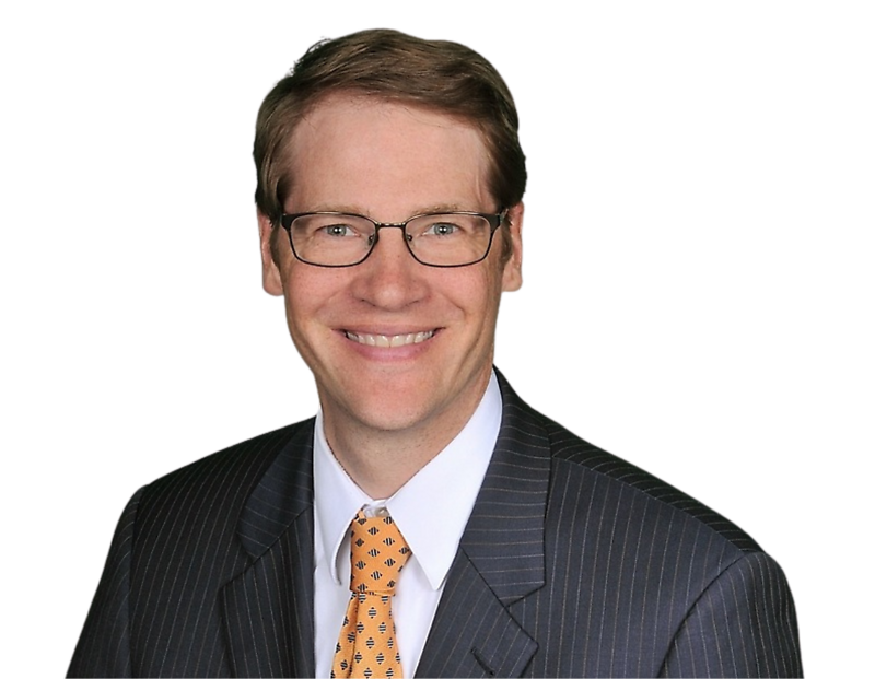 A smiling man in a dark pinstripe suit, white dress shirt, and orange patterned tie poses against a plain background. He has short light brown hair, wears rectangular glasses, and appears in a professional headshot.