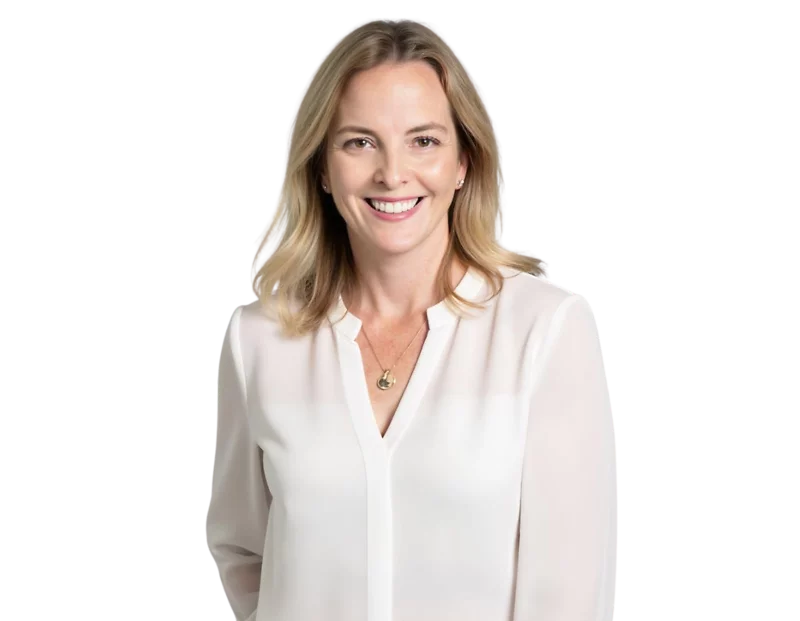 A woman with shoulder-length blonde hair smiling warmly in a professional headshot. She is wearing a white blouse and a gold pendant necklace, posed against a plain background.