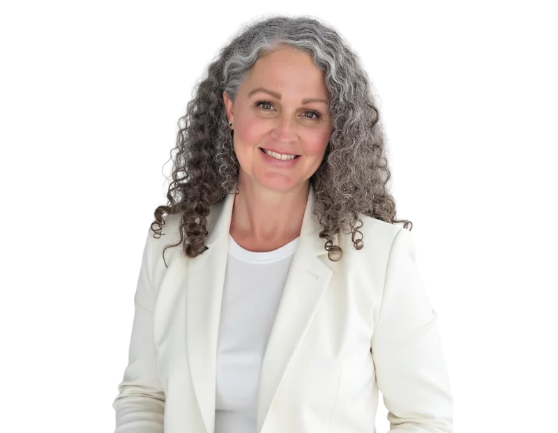 A woman with long, curly gray hair and a warm smile is wearing a white blazer over a white top. She is facing the camera with a confident and approachable expression, set against a transparent background.