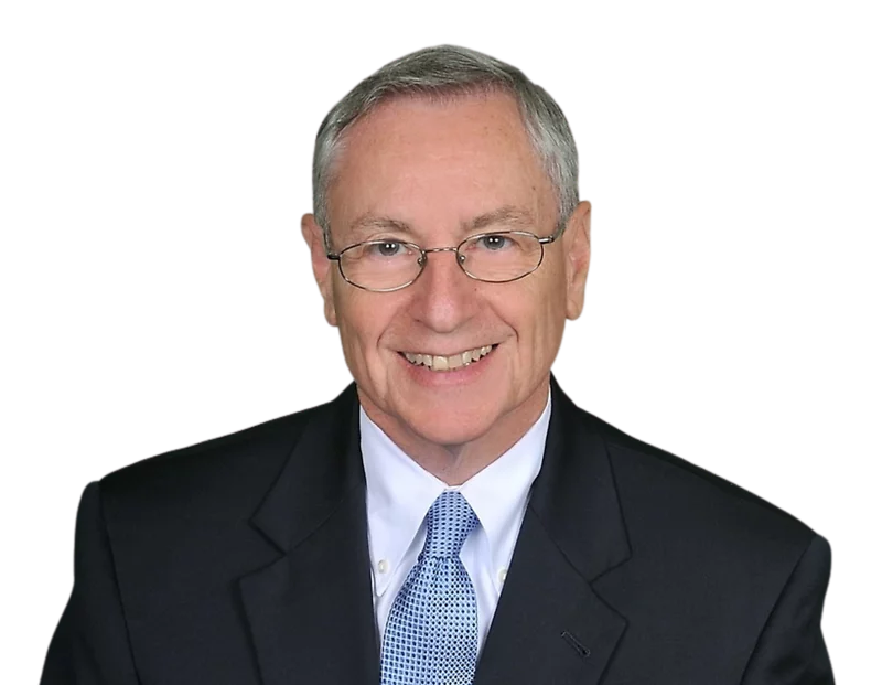 Professional older man with short gray hair and glasses, smiling in a dark suit, white shirt, and light blue tie.
