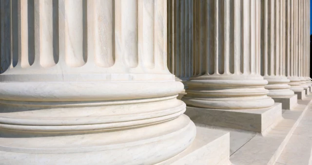 Close-up view of the marble bases of large fluted columns, showing their smooth, rounded detailing and sturdy architectural design. The perspective emphasizes strength, stability, and the grandeur of classical architecture often seen in government.