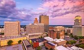 Downtown Winston-Salem, North Carolina, at sunset with a colorful sky casting warm light on its mix of historic and modern buildings. The distinctive rounded dome of the Winston Tower stands out among the skyline.