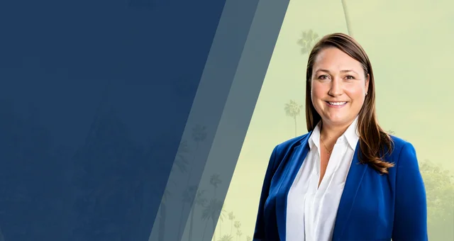 Michelle Meek smiles in a professional headshot, wearing a white blouse and royal blue blazer. She stands against a background with tall palm trees and angled color blocks, suggesting a California setting.