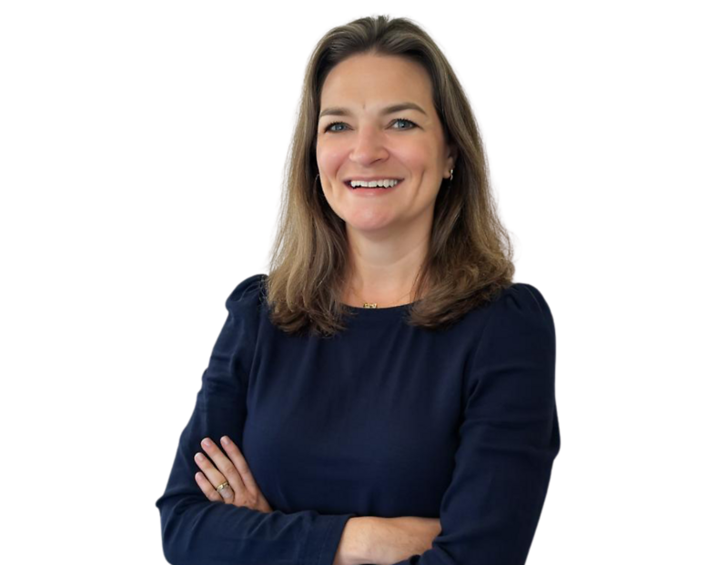 Professional head-and-torso portrait of Missy Spainhour, smiling with her arms crossed. She is wearing a dark long-sleeved top and standing against a light, modern background with soft blue geometric accents.