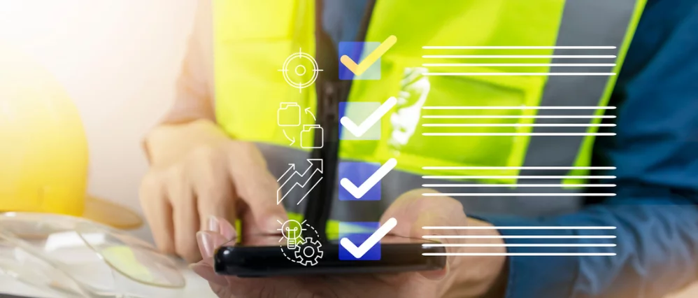 Close up of a worker wearing a high visibility safety vest using a tablet, with transparent checklist icons and progress symbols overlaid on the screen. White check marks, target, growth chart, and gear icons appear beside horizontal lines, suggesting com