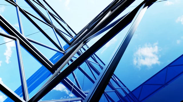 Upward view of a modern glass and steel building with angular beams reflecting the blue sky and scattered clouds. The structure's geometric lines create a dynamic, futuristic perspective.