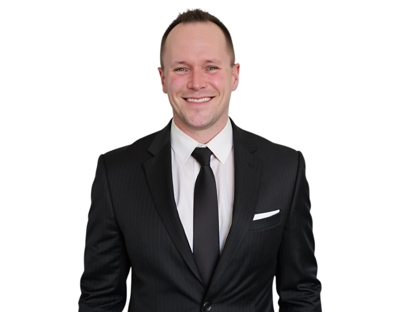 Smiling professional man with short light hair wearing a black pinstripe suit, white dress shirt, and solid black tie, with a white pocket square. He stands confidently against a transparent background, presenting a sharp and formal business appearance.