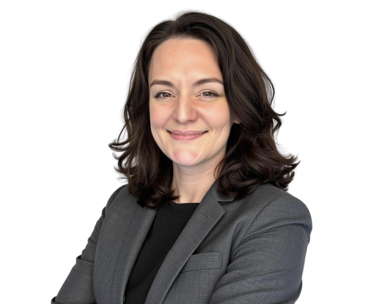 Smiling professional woman with shoulder-length dark wavy hair wearing a gray blazer over a black top, standing with arms crossed against a transparent background. Her expression is friendly and confident, projecting a composed and competent business pres