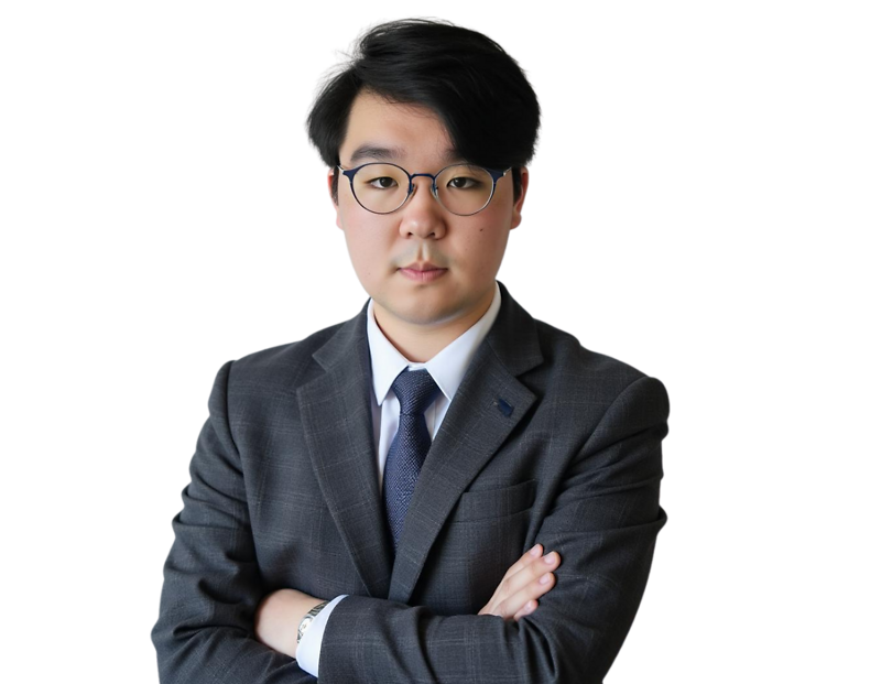 Professional man with short black hair and round glasses wearing a gray suit, white dress shirt, and dark blue tie, standing with arms crossed against a transparent background. He has a serious, focused expression that conveys professionalism and confiden