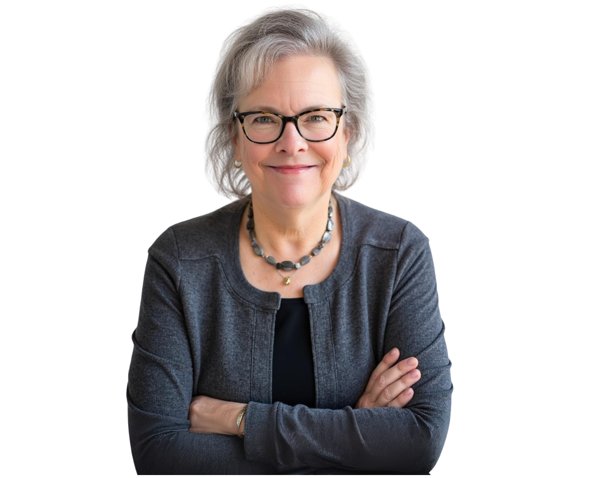 Smiling older woman with short gray hair and glasses, wearing a dark gray cardigan over a black top and a beaded necklace, with arms confidently crossed. She has a warm, approachable demeanor and a professional presence against a transparent background.