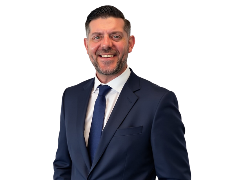 Smiling professional man with short dark hair and a neatly trimmed beard wearing a navy blue suit, white dress shirt, and matching blue tie. He stands against a transparent background with a friendly and confident expression suited for a corporate or exec