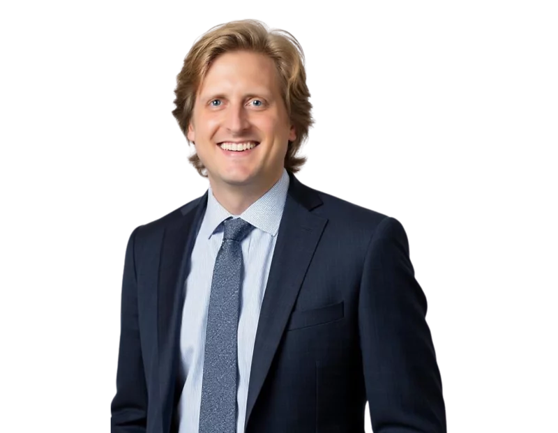 Evan Jarrold smiling in a dark navy suit with a light blue shirt and patterned tie, posed against a transparent background in a professional headshot style.
