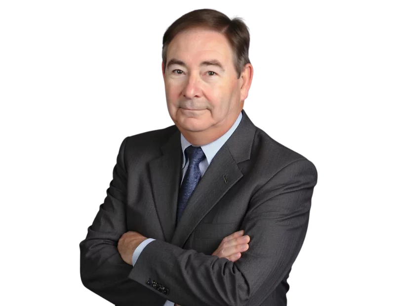 Rick Brown in a dark gray suit and blue tie standing with arms crossed, looking confidently at the camera against a transparent background. His expression is calm and professional, suggesting a business or executive portrait.