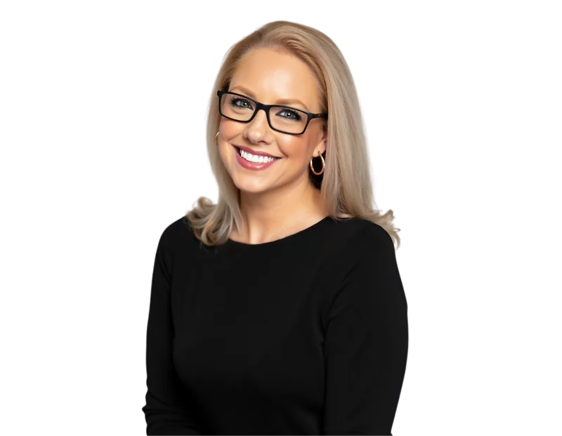 Leigh Tyson wearing black-rimmed glasses, gold hoop earrings, and a black top, posed against a transparent background. Her arms are gently folded and she’s looking directly at the camera with a confident, friendly expression.